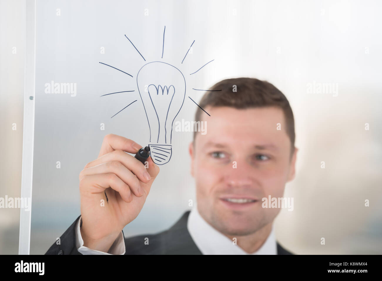 Smiling Mid Adult Businessman Drawing Lightbulb On Glass Wall In Office