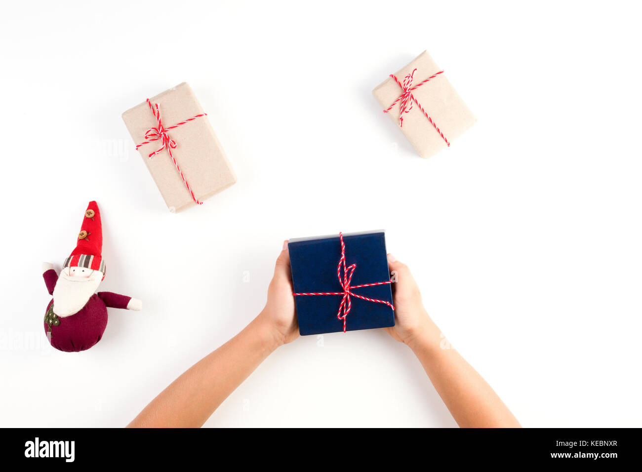 Top View Of Kid Hands Holding A Present Gift Boxes Packed In Craft Paper And Christmas Decoration On White Table Top View Of Kid Hands Holding A Present Gift Boxes Packed In Craft Paper And Christmas Decoration On White Table
