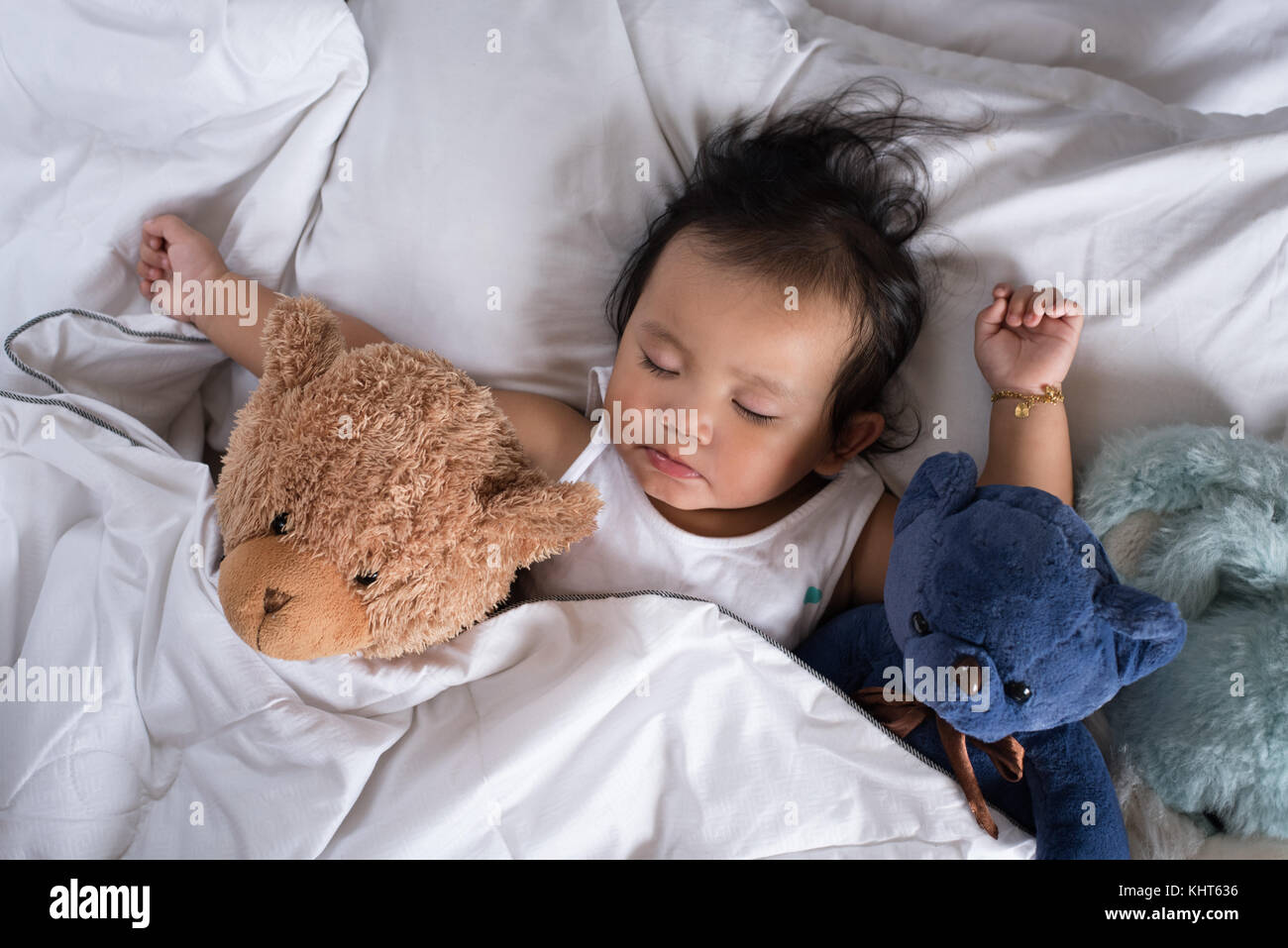Asian Toddler Sleeping With Teddy Bear On White Bed Pillow And