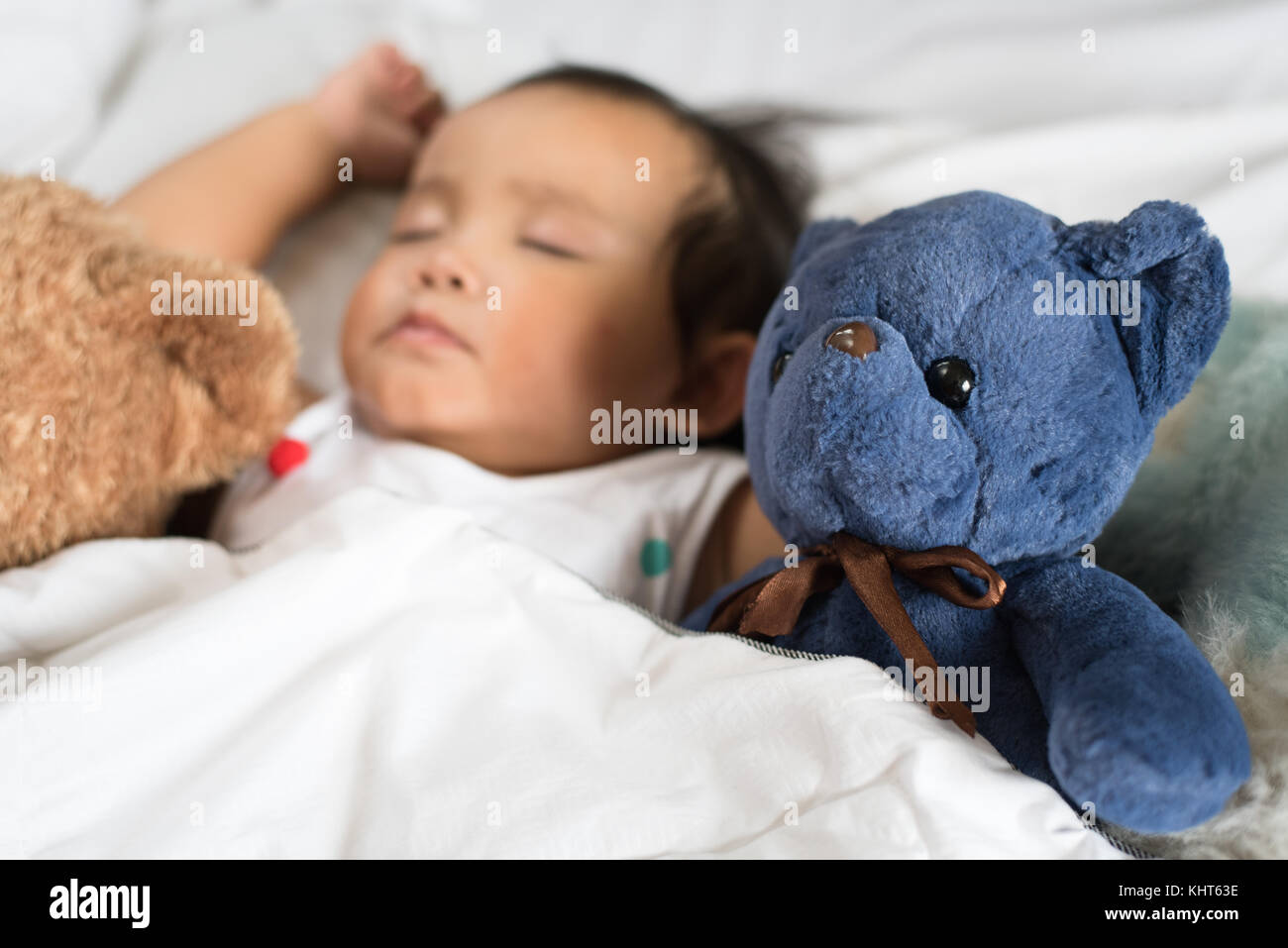 Asian Toddler Sleeping With Teddy Bear On White Bed Pillow And