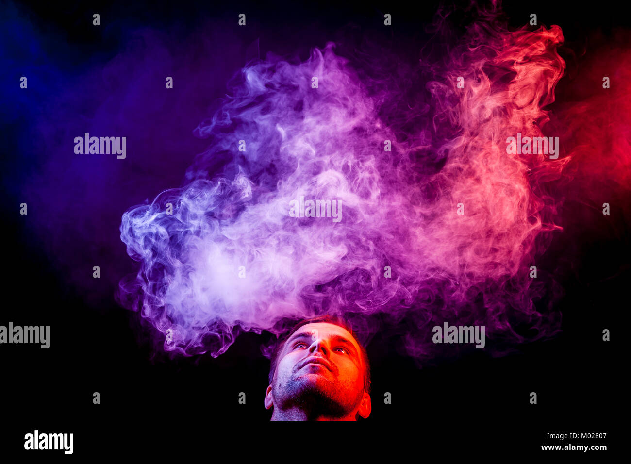 a young man exhales a cloud of colored smoke of blue and pink color vapor color
