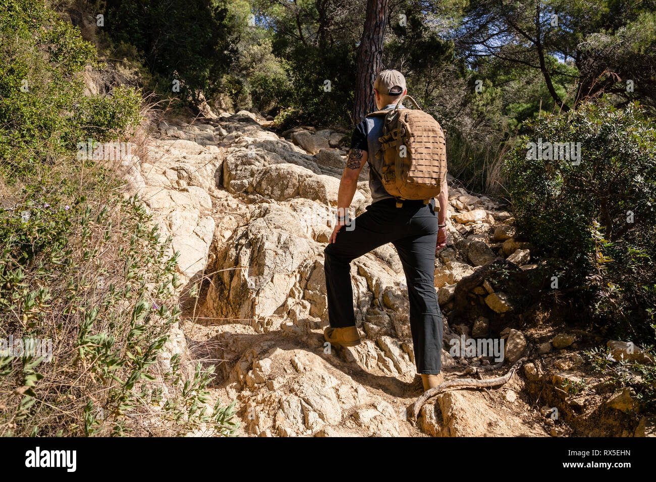 A Man With Backpack Hiking On A Path Of Rocks In A Forest With Sunlight