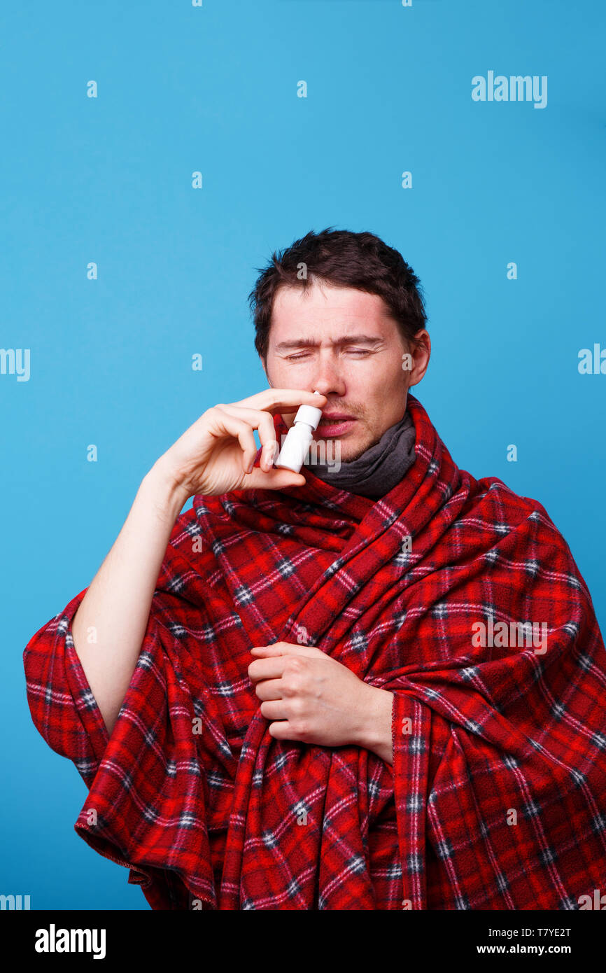 A Wrapped In A Blanket Sick Man Is Standing And Using Nasal Spray Stock