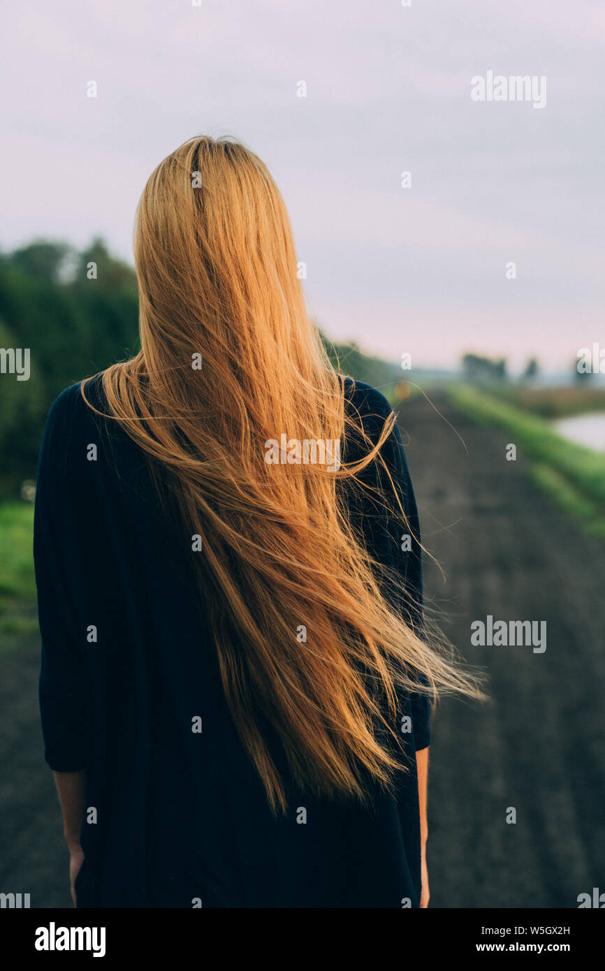 Woman With Very Long Hair Standing Back To Camera On Country Road Stock