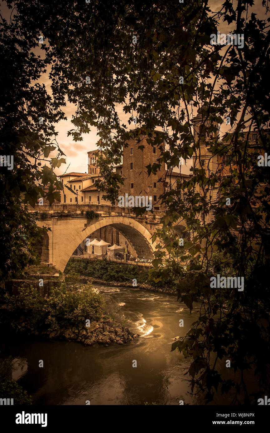 Old Arch Bridge Over Canal Seen Through Trees During Sunset Stock Photo