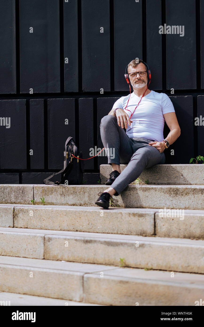 Bearded Mature Man Sitting On Steps With Headphones While Relaxing On A