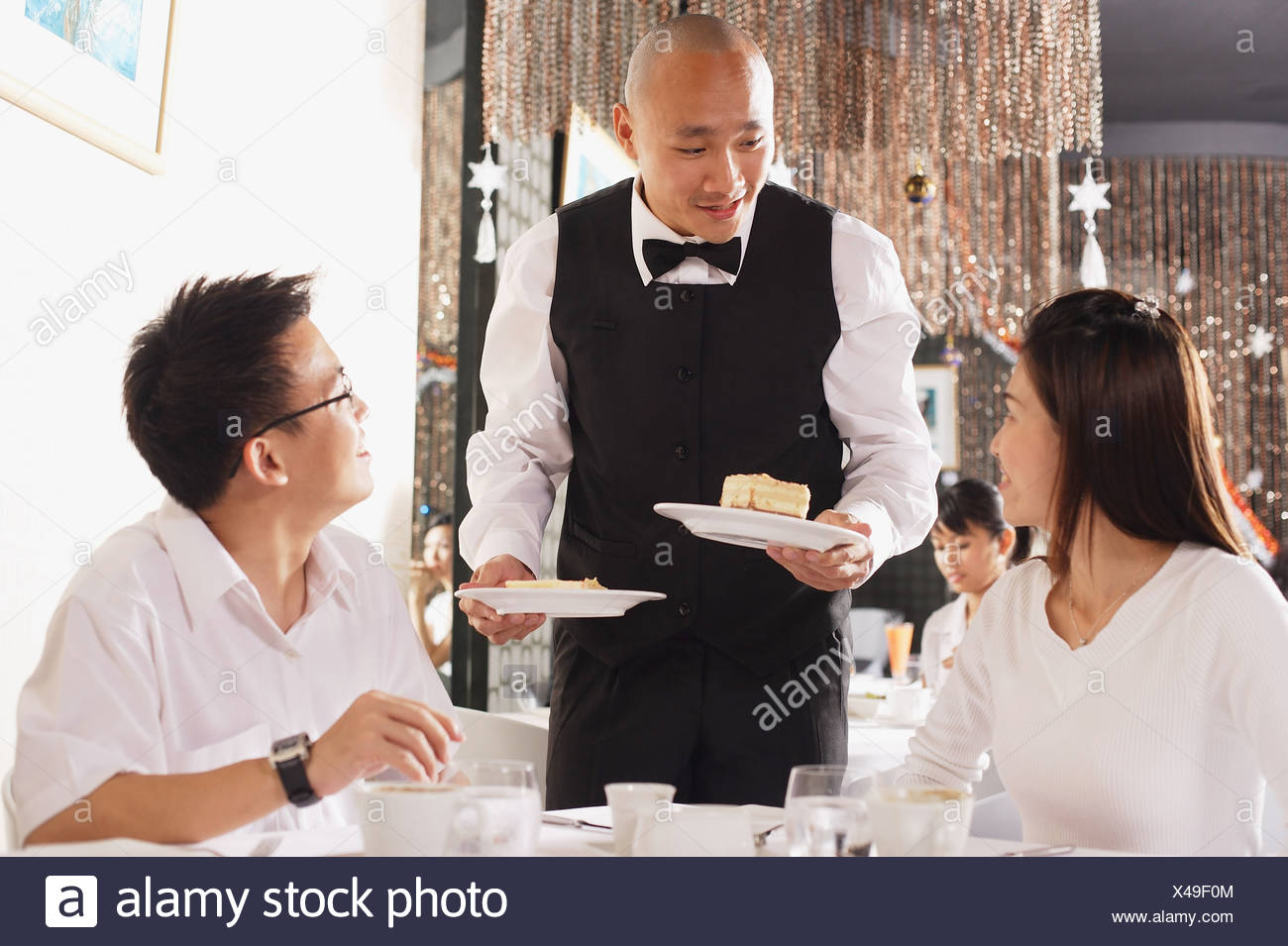 couple in restaurant waiter standing holding plates of dessert