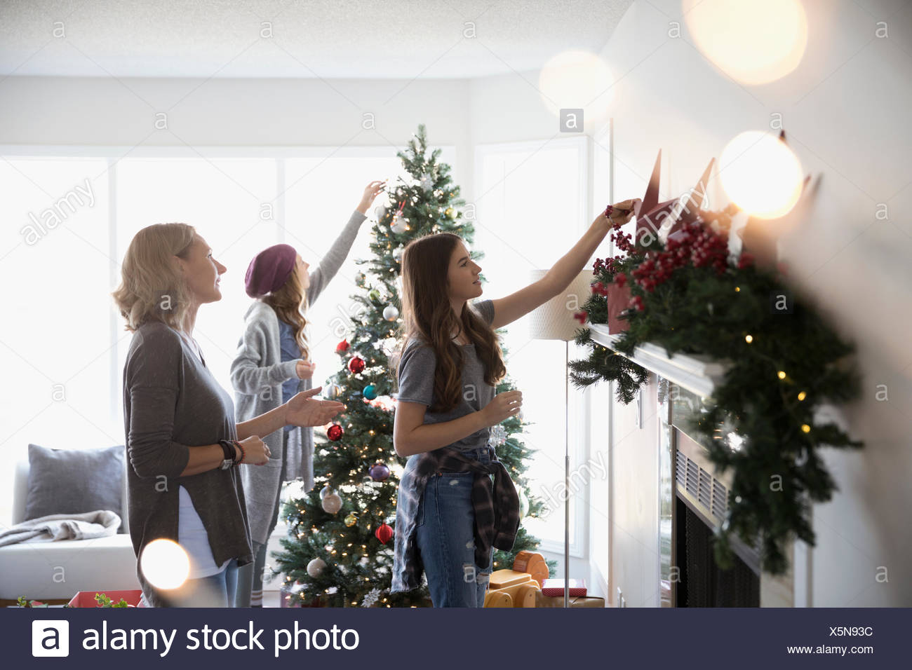 mother and daughters decorating christmas tree and hanging garland on fireplace mantle in living room - Hanging Garland Christmas Decorations mother and daughters decorating christmas tree and hanging garland on fireplace mantle in living room - Hanging Garland Christmas Decorations