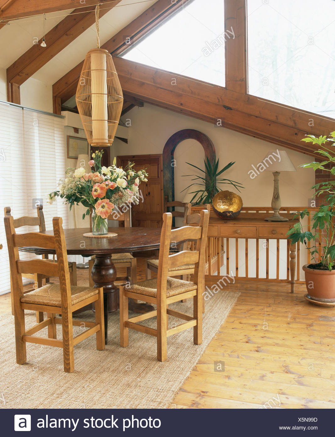 Cylindrical Light Above Circular Mahogany Dining Table And Rush Seated Chairs In Upstairs Room With Rug On Wooden Floor Cylindrical Light Above Circular Mahogany Dining Table And Rush Seated Chairs In Upstairs Room With Rug On Wooden Floor