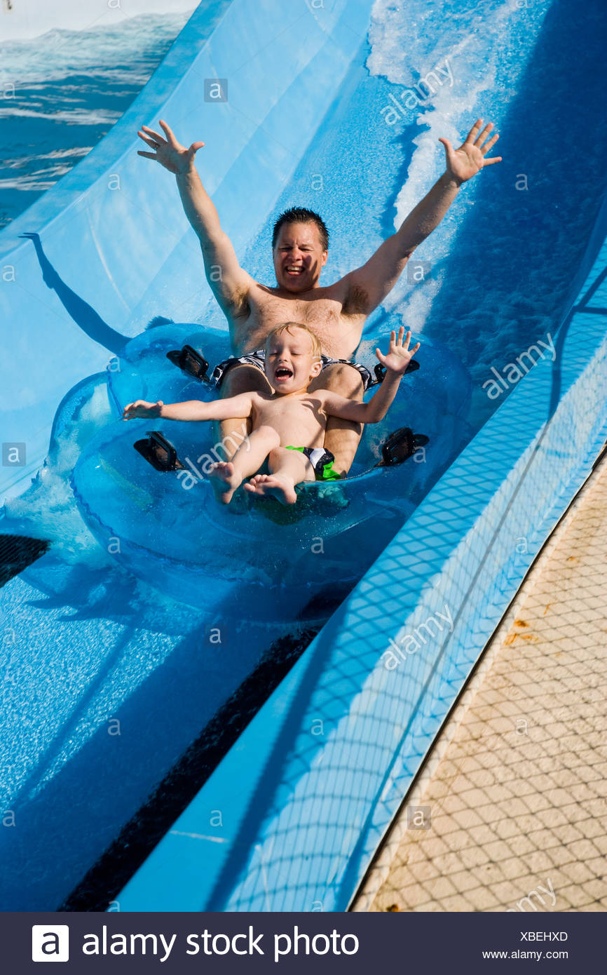 Father And Son Sliding Down Water Slide Together On Innertube In Water Park Father And Son Sliding Down Water Slide Together On Innertube In Water Park