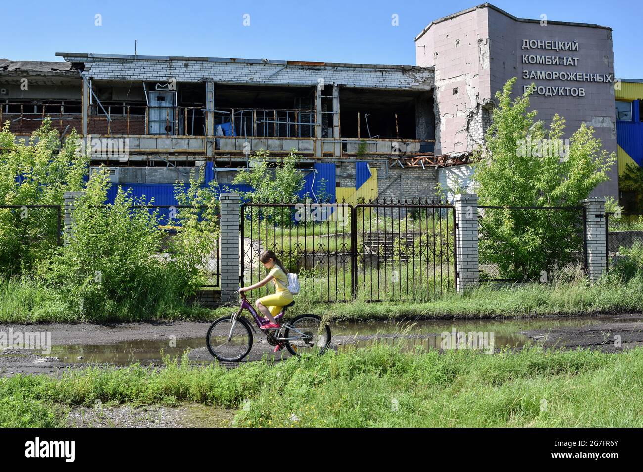 Ein Mädchen das mit dem Fahrrad an einer zerstörten Fabrik in Marinka