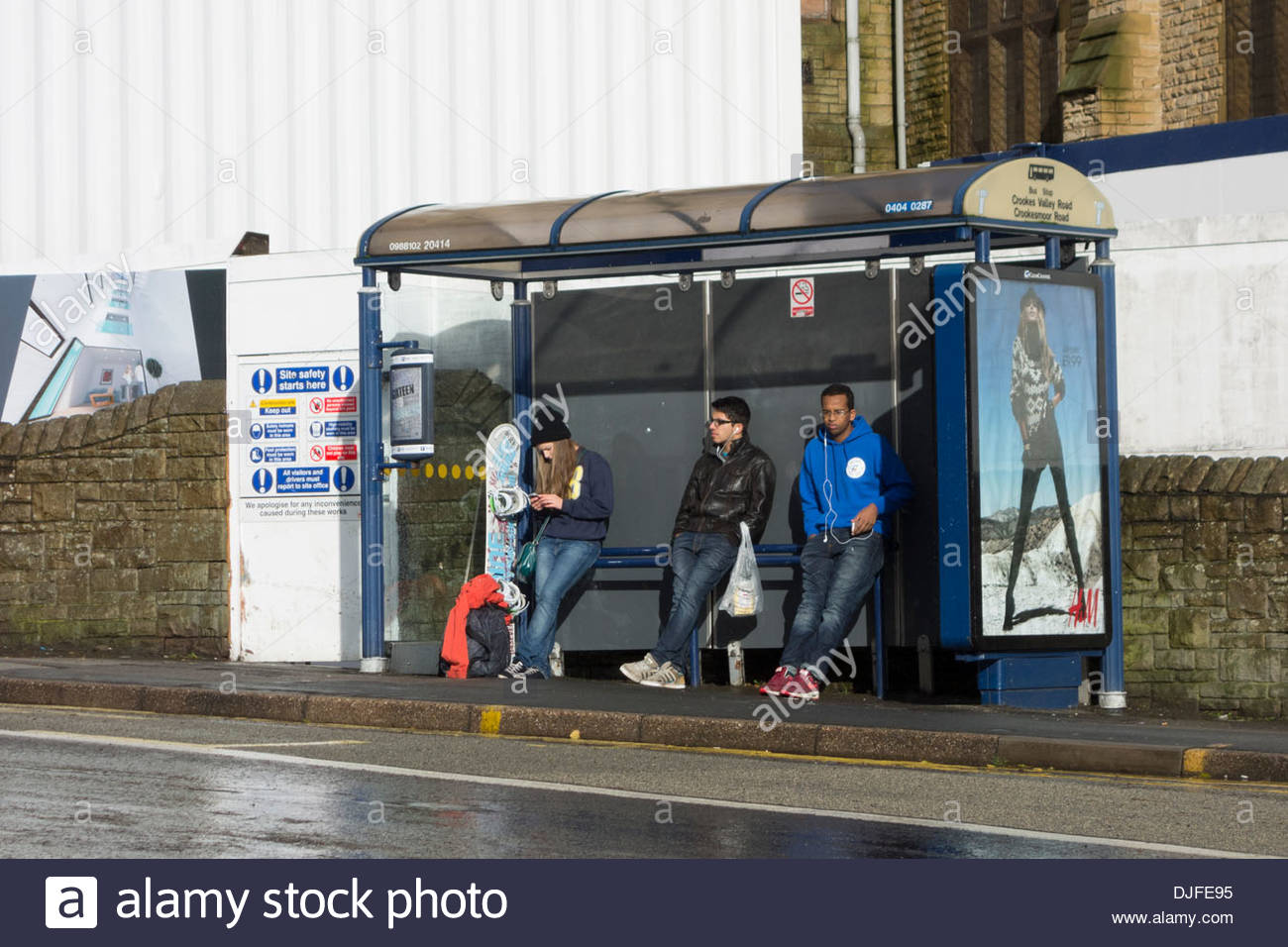 Drei Menschen warten auf einen Bus in einer Bushaltestelle in Sheffield