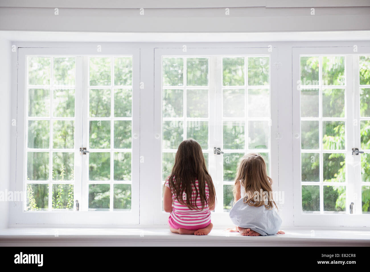 Zwei Mädchen sitzen nebeneinander durch ein großes Fenster