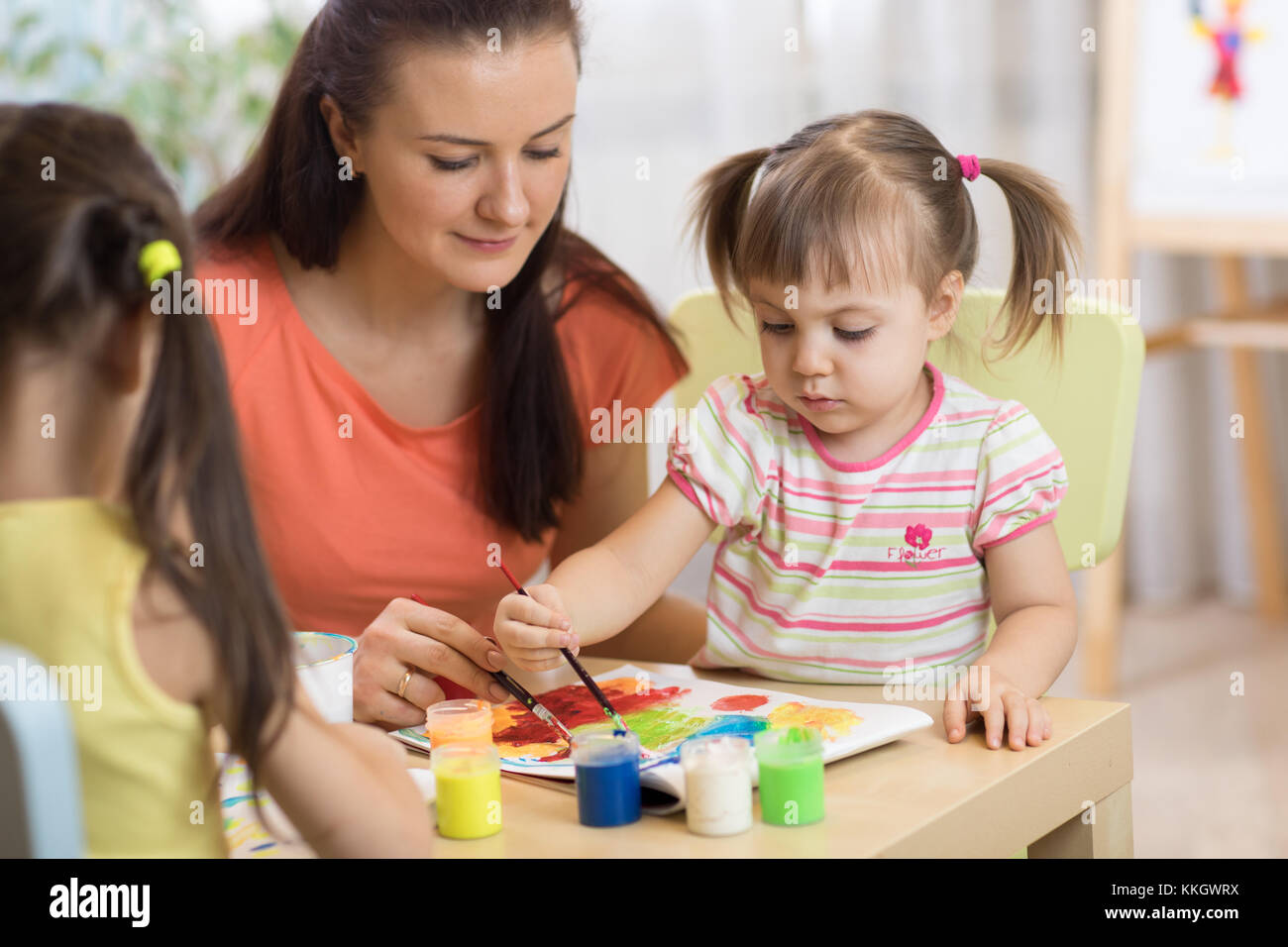 Kinder malen im Kindergarten Lehrerin hilft durch kleines Mädchen