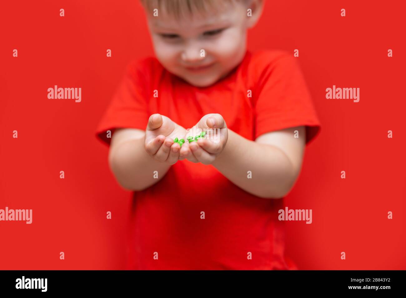 pequeño niño triste llevar muchas píldoras en las manos camiseta roja