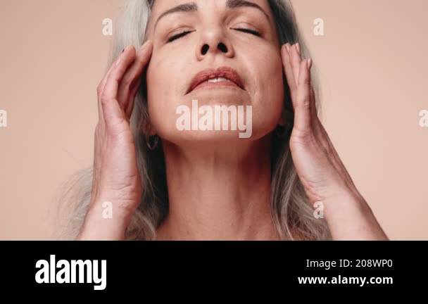 A serene middle age woman with eyes closed, touching her face gently to ...