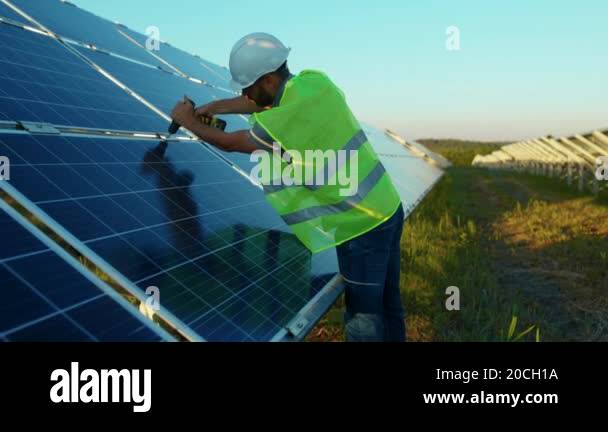 Man worker fixing solar panel to a metal basis with a drill in a sunny ...