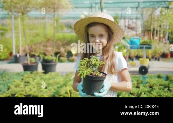 Portrait of happy small girl in standing holding pot plant smiling look ...