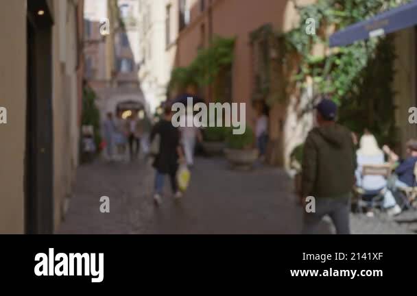 Blurred scene of people walking down a narrow cobblestone street in ...