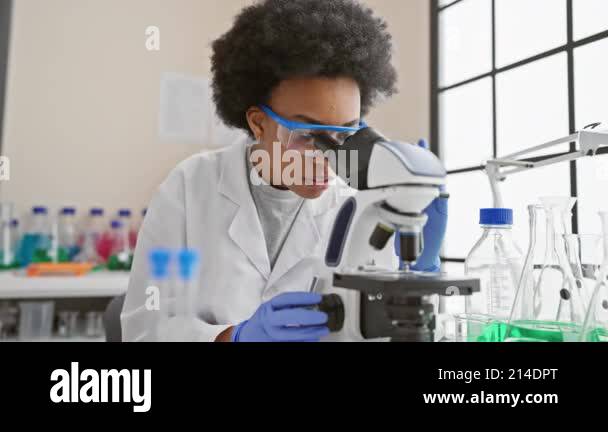 African woman scientist examining sample under microscope in lab Stock ...
