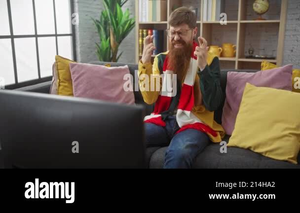 Young bearded redhead man exulting while watching tv in a cozy living ...