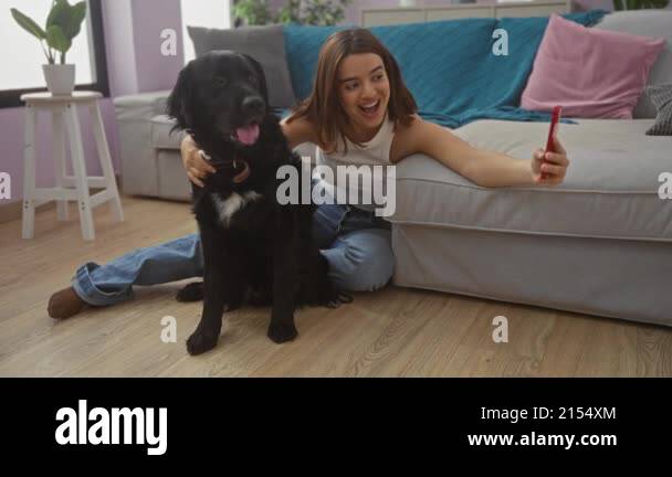 A young woman takes a selfie with her black labrador dog in a cozy ...