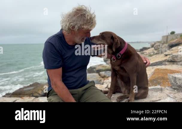 portrait of senior latino man bonding with his dog outdoors with ocean ...
