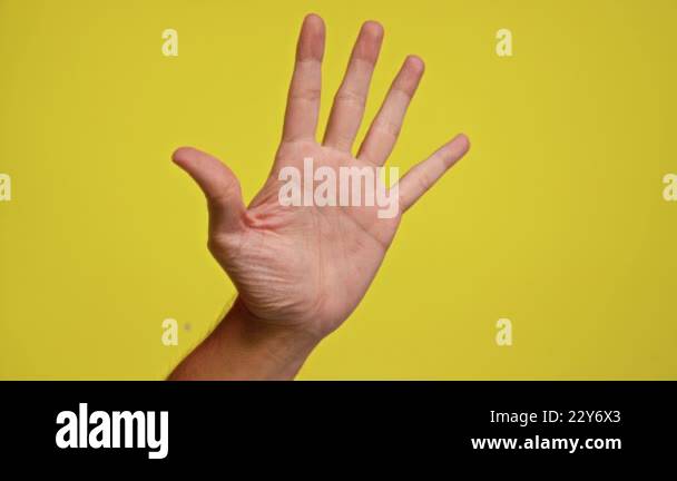 Male hand raised against a bright yellow background demonstrating an ...