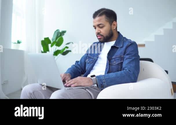 serious african american man uses a laptop and types online at home ...