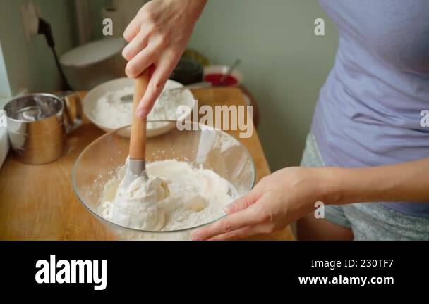 Woman mixing flour and batter in glass bowl using wooden spatula during ...