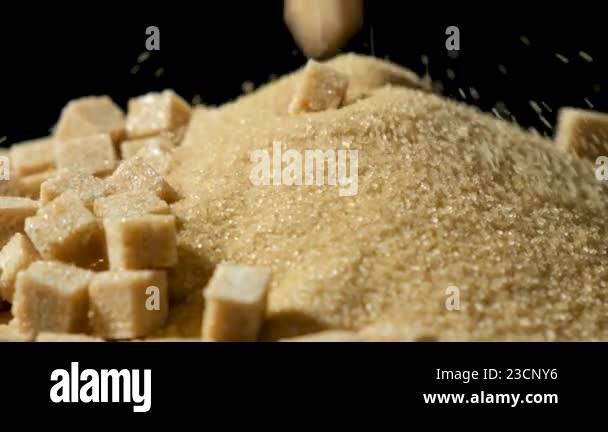 Cane sugar cubes falling into a pile of crystalline brown sugar, slow ...