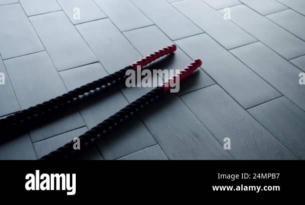 Close-up of red and black battle ropes on a gray gym floor, symbolizing ...