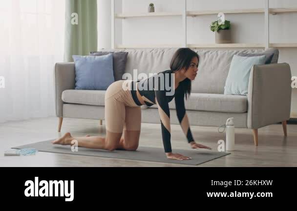 A young African American woman is exercising on a yoga mat in her ...