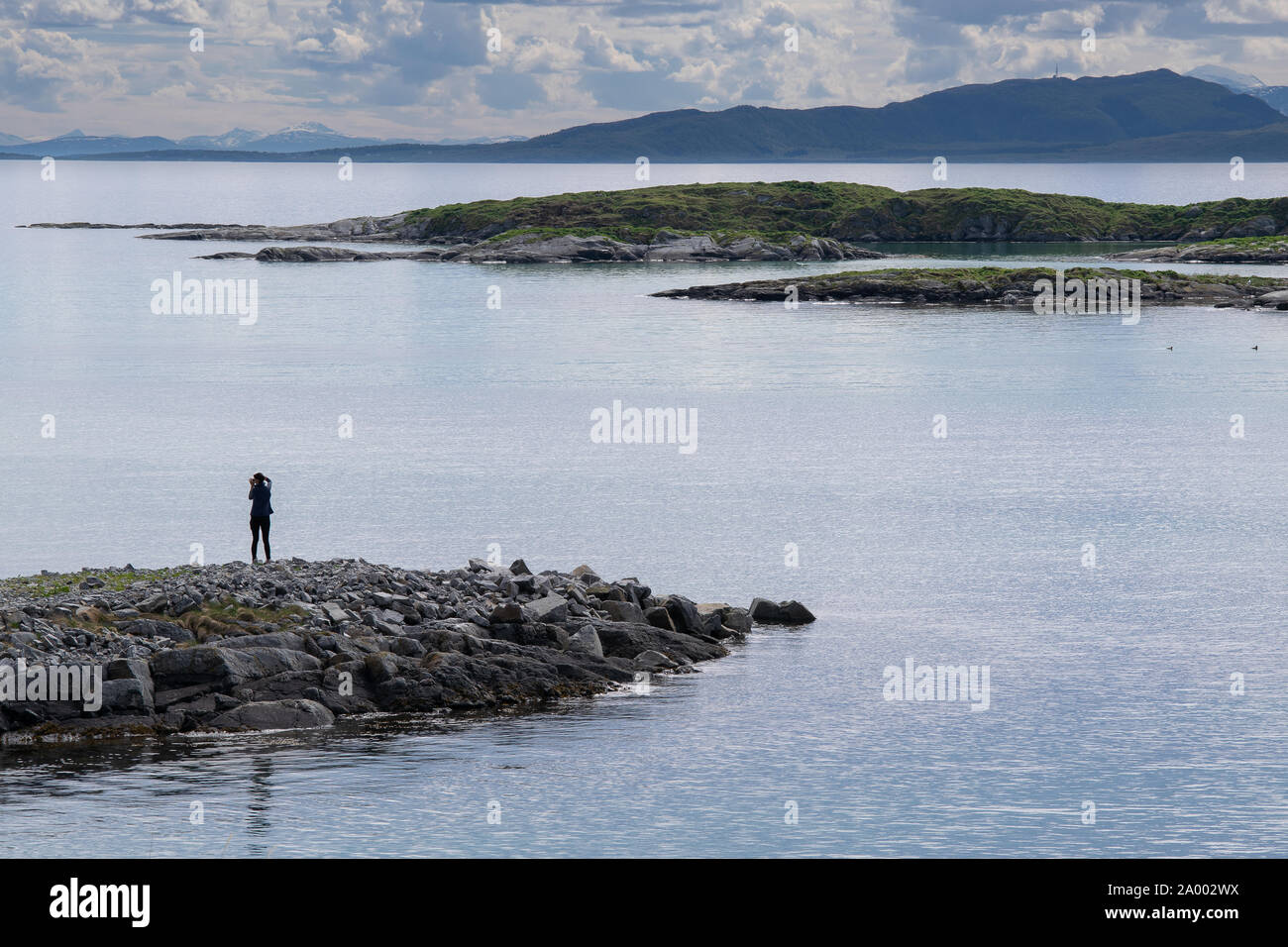 An active and attractive woman photographs the breathtaking mountains and scenery of the coastline of the island of Senja in northern Norway. Stock Photo