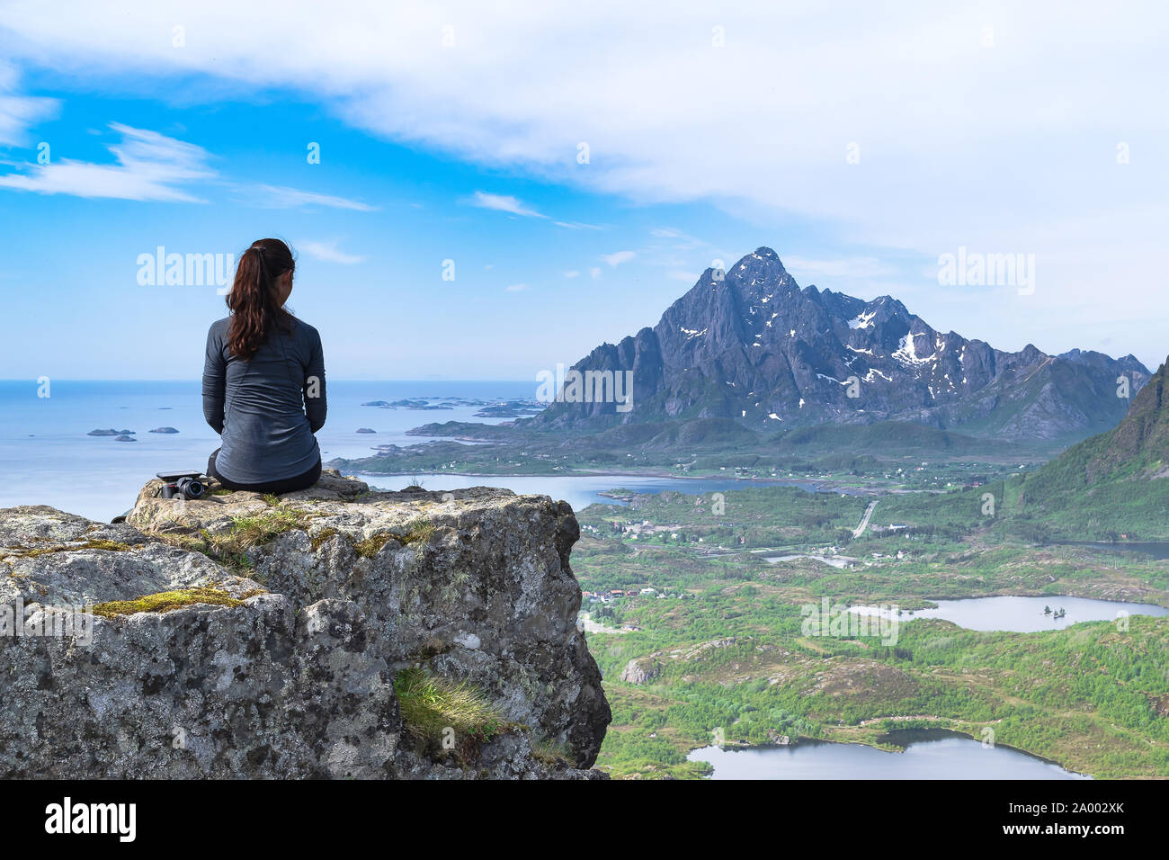 An athletic and attractive woman ponders the incredible scenery of the Lofoten Islands from atop a mountain above the towns of Kabelvag and Svolvaer. Stock Photo