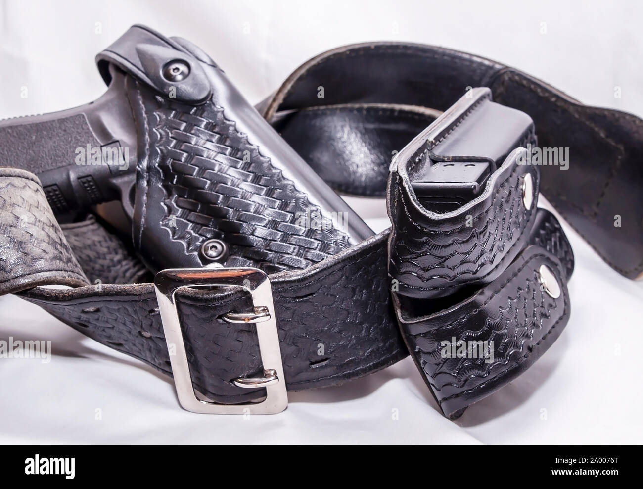 A worn police duty belt with a black pistol and two pistol magazine case wrapped up on a white background Stock Photo