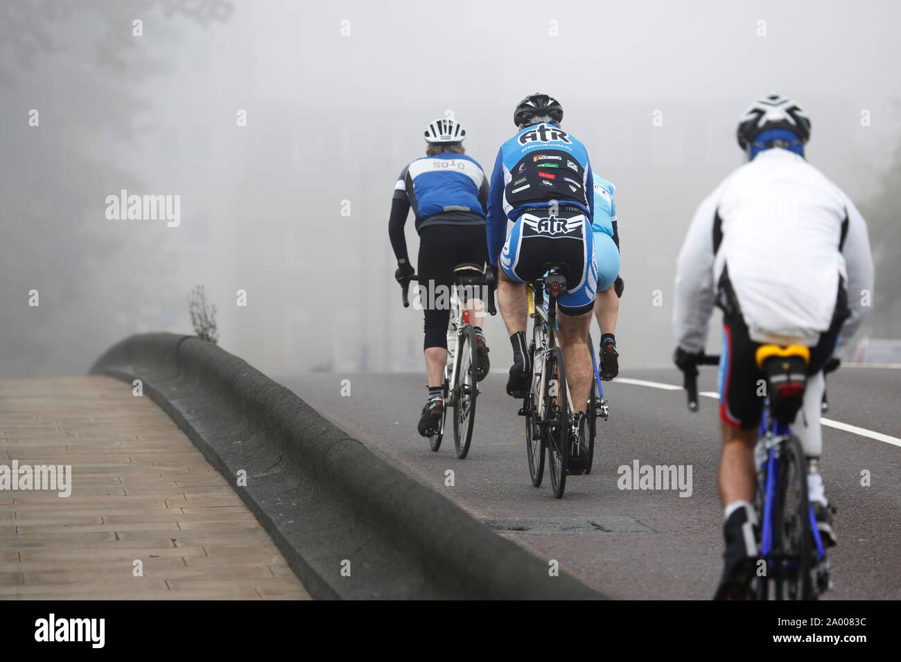 Cyclists riding, bicycle commuters, in heavy fog, a cold bad weather day. Stock Photo