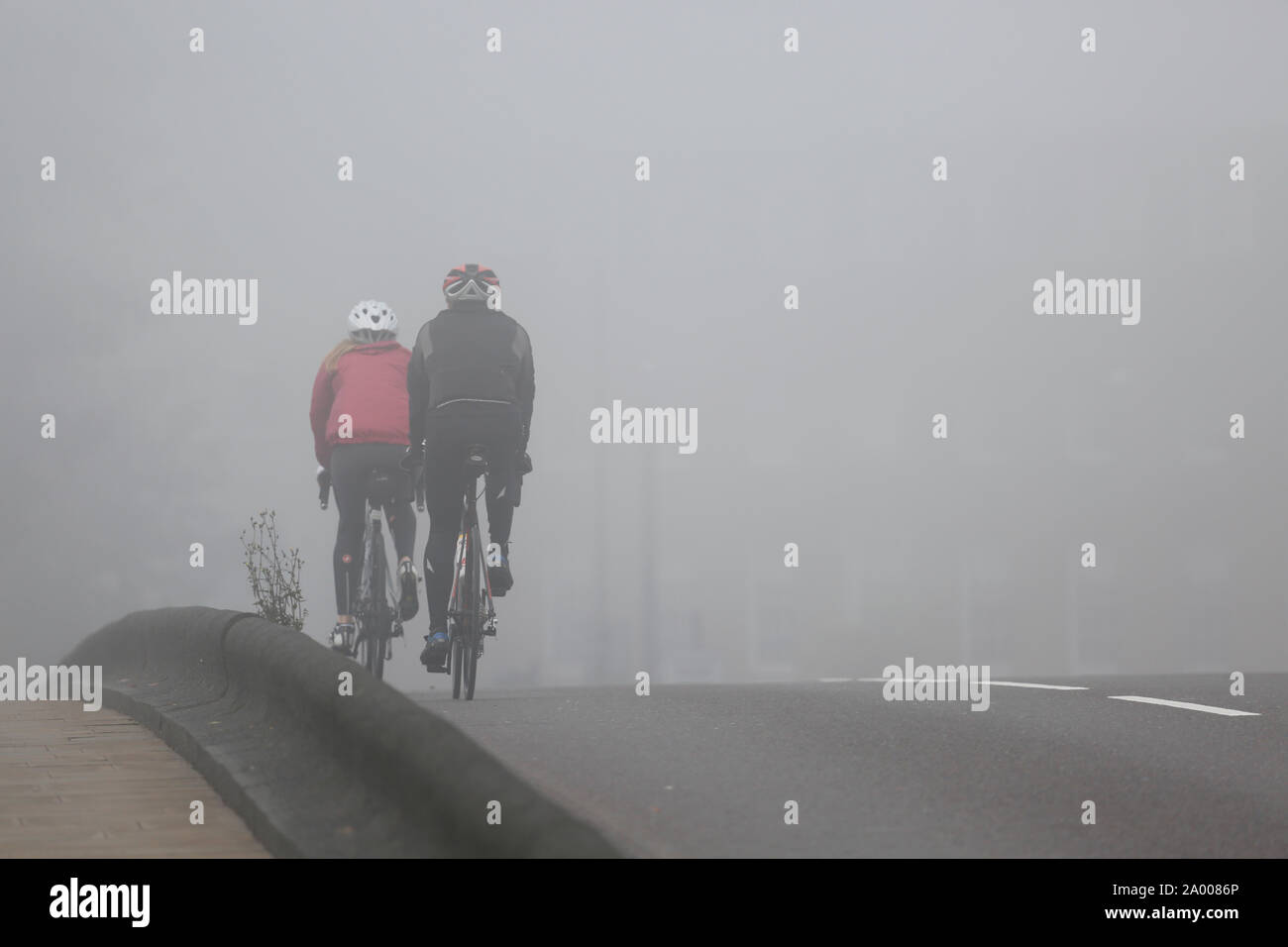 Cyclists riding, bicycle commuters, in heavy fog, a cold bad weather day. Stock Photo