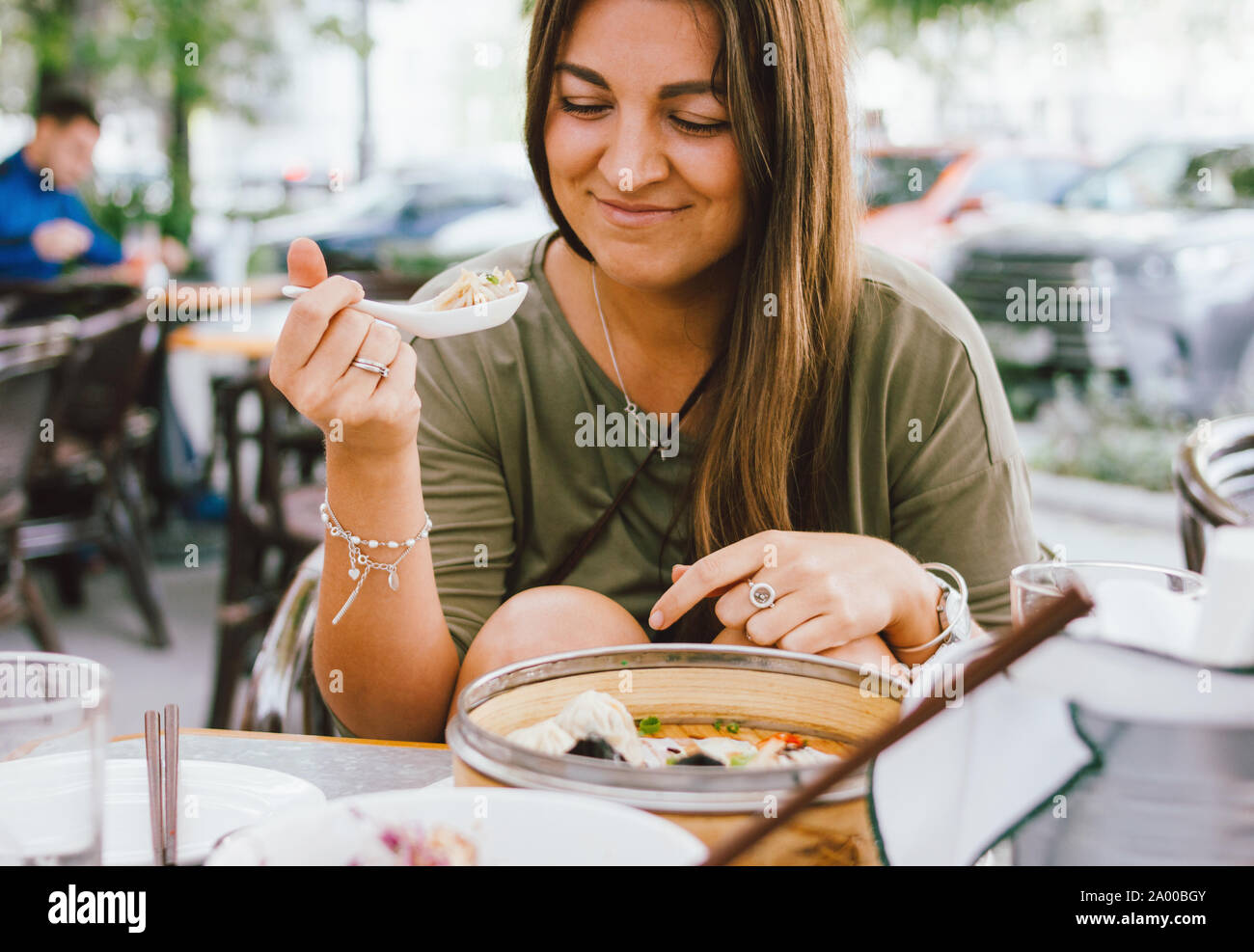 Young smiling brunette girl eating dim sum in a street cafe Stock Photo