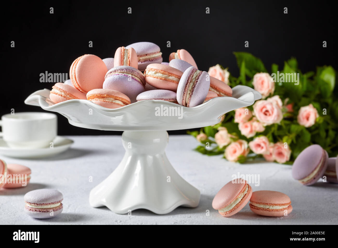 close-up of macarons on a white cake stand. beautiful bouquet of roses and cup of coffee at the black background, free space Stock Photo
