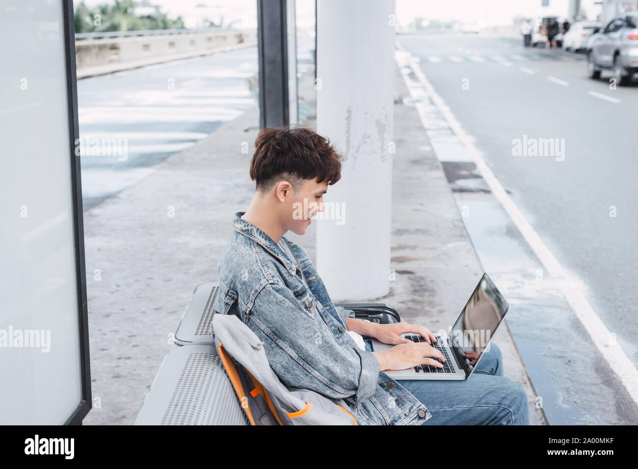 Asian hansome guy is working on a portable computer connected to public wi-fi while sitting on the chair at the airport bus stop Stock Photo