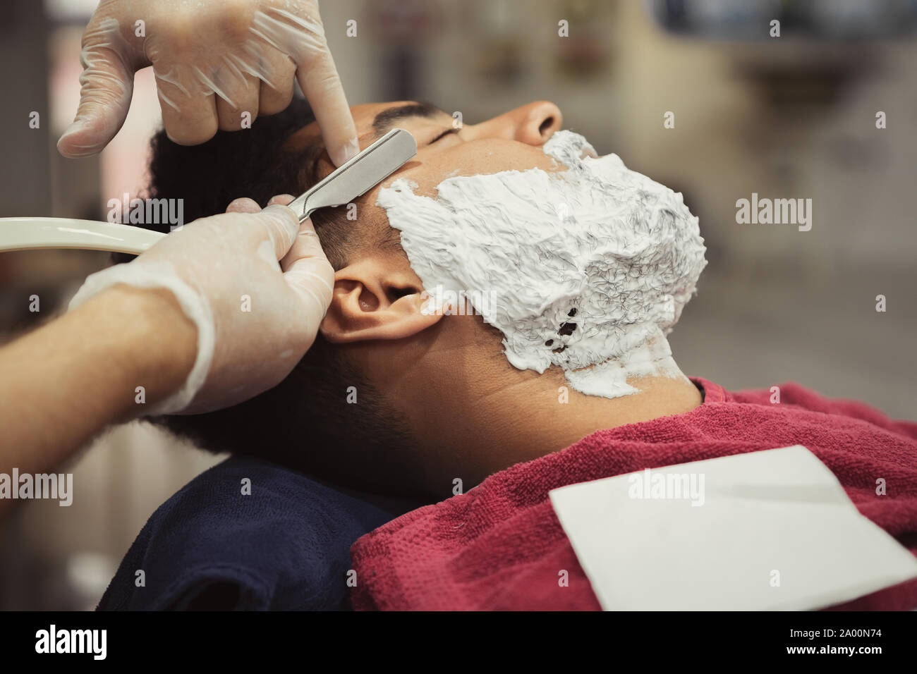 Professioinal barber shaving client with razor in beauty salon.Young