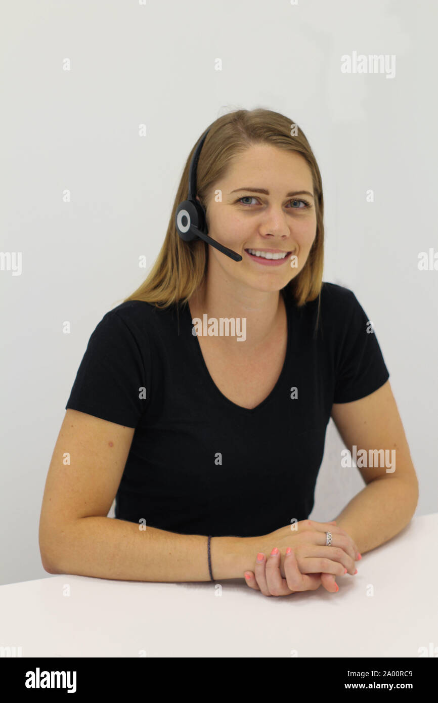 Portrait of a young woman wearing a headset. The woman is sat face on, smiling, with a plain background behind her. Stock Photo