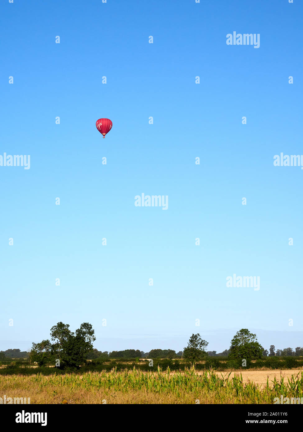 A red hot air balloon over farmland near Grantham in Lincolnshire against the vibrant clear blue sky Stock Photo