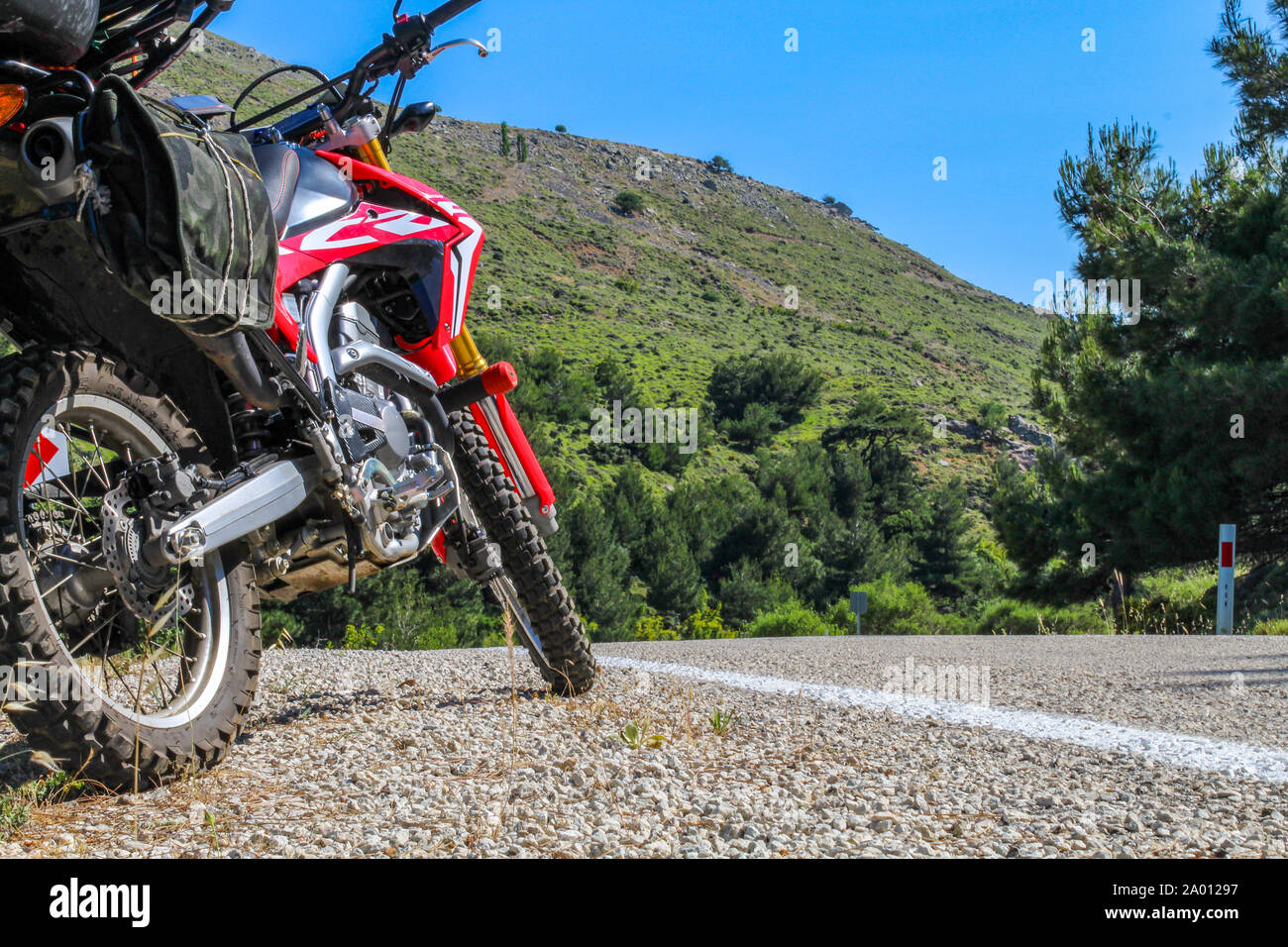 A red enduro motorcycle parked  on the gravel road on the side of the asphalt road. Only gear tire and mechanical parts are in the frame Stock Photo