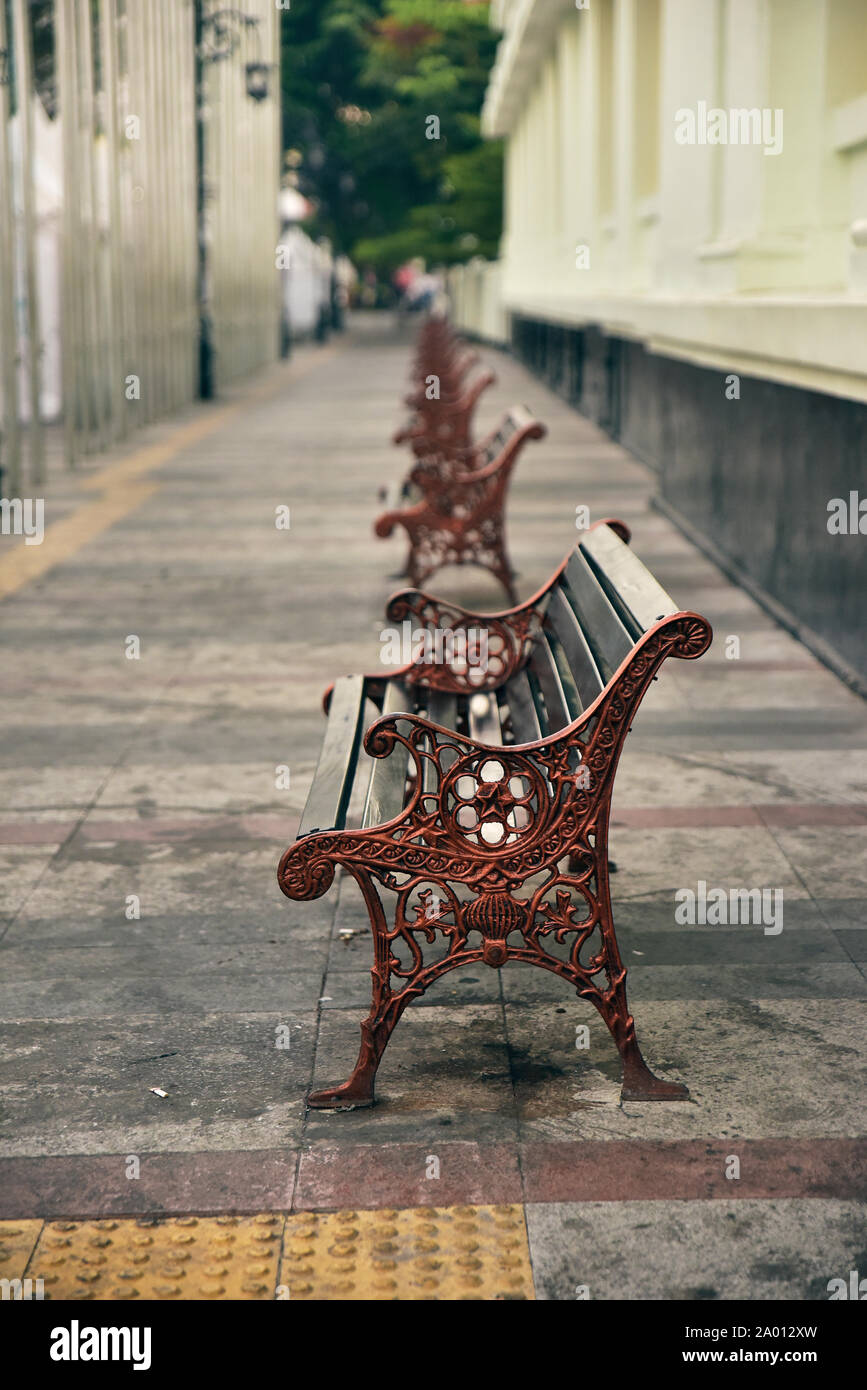 A row of Classic Wooden bench with iron black legs on a stone sidewalk city Stock Photo