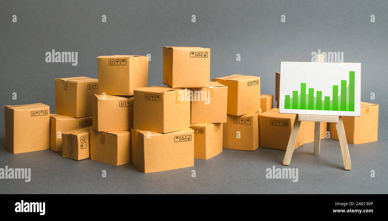 A large number of cardboard boxes and sign with green positive trend chart. rate growth of production of goods and products, increasing economic indic Stock Photo