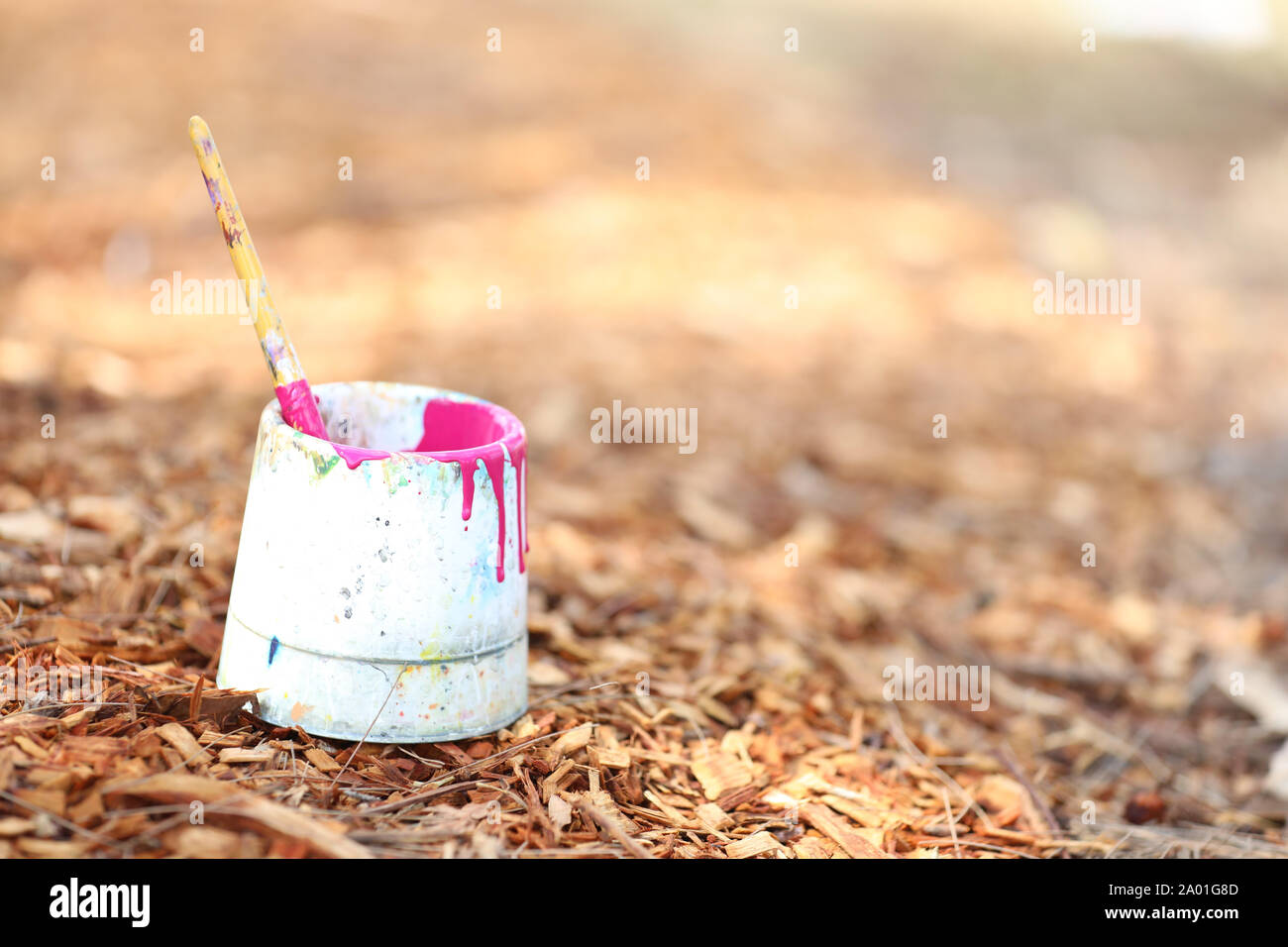 single paintbrush in a white paint tub. Bush, mulch, wood chip background. Creative potential concept or theme. Bright fluorescent fluro pink magenta Stock Photo