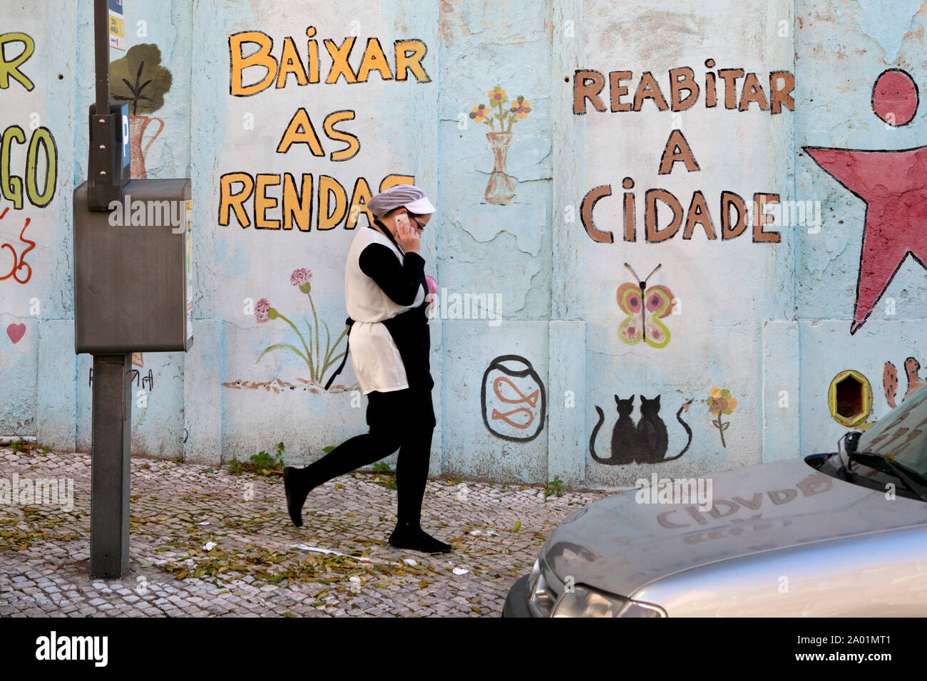 LISSABON - A shop assistent walks past a text on a wall that reads: Lower the rents and make the city liveable. Stock Photo