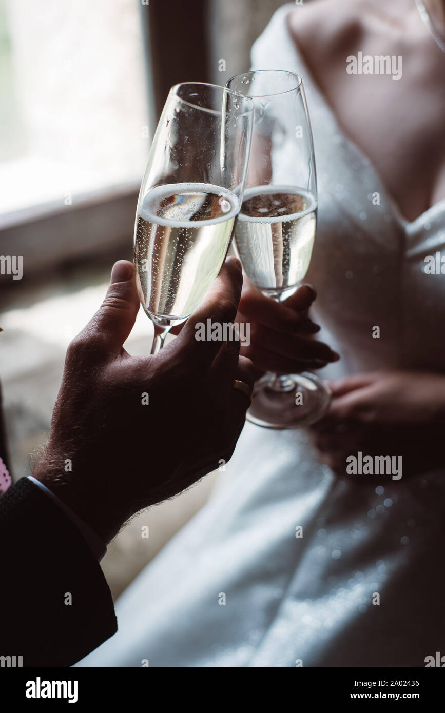 Close up of married couple toasting champagne glasses at wedding party. Hands bride and groom clinking glasses at wedding reception. Stock Photo